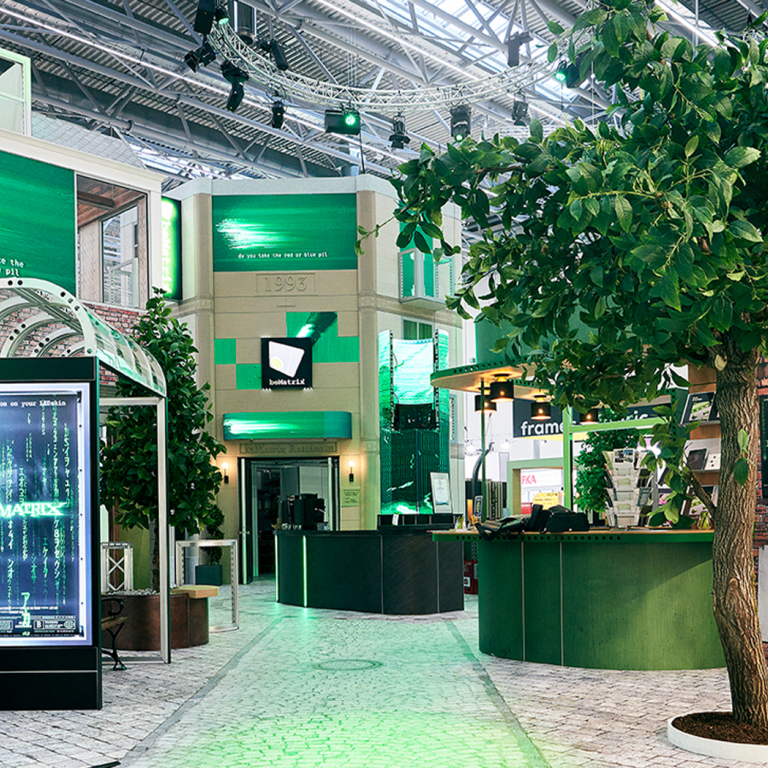 A modern indoor space with green lighting, digital screens displaying code, plants, and a curved green reception desk, creating a tech-inspired, futuristic atmosphere.