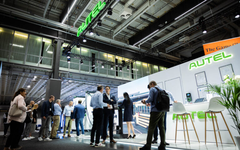 People gather and interact at a modern trade show booth with the brand name Autel prominently displayed above and on the walls. The scene is lively, with bright lighting and a spacious, high-ceilinged exhibition hall.