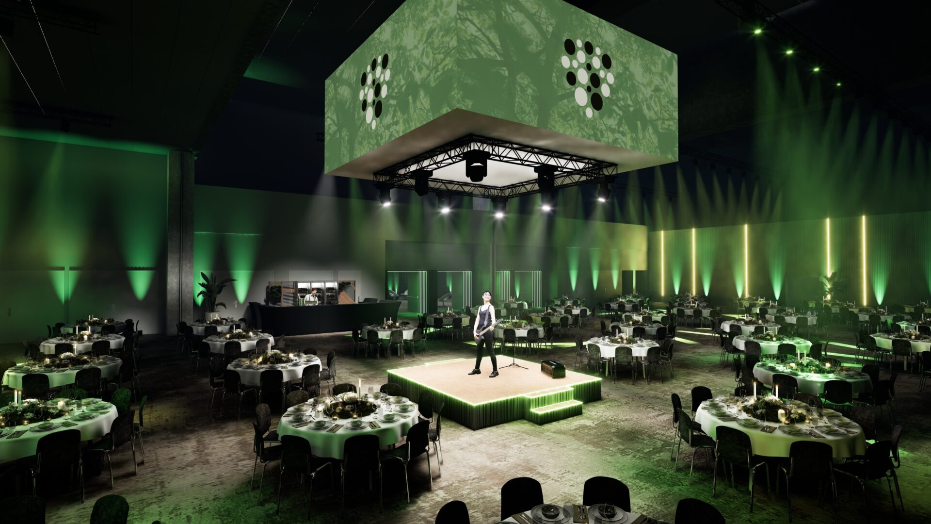 A large banquet hall with round tables set for dinner, green lighting, and a stage in the center where a person stands under spotlights. A suspended cube with lights hangs above the stage, creating a modern atmosphere.