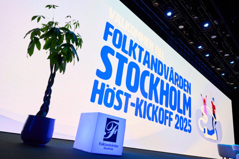 A large screen displays “Välkommen till Folktandvården Stockholm Höst-Kickoff 2025” in blue text, with a potted plant and a Folktandvården Stockholm podium in the foreground.